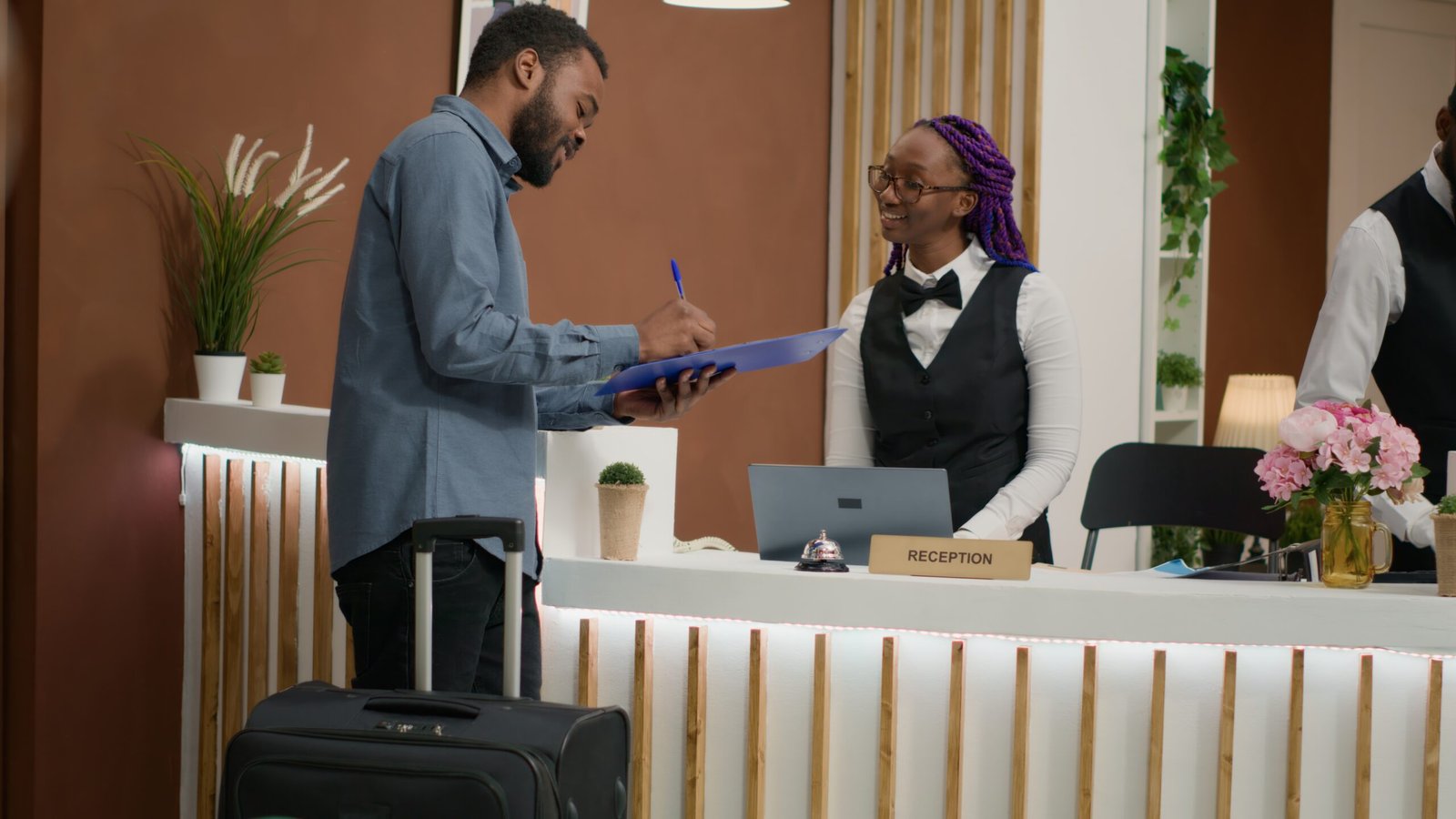 Guest filling in registration forms and signing papers before seeing room, finishing with check in. Employee providing luxurious concierge services, greeting people at front desk. Handheld shot.
